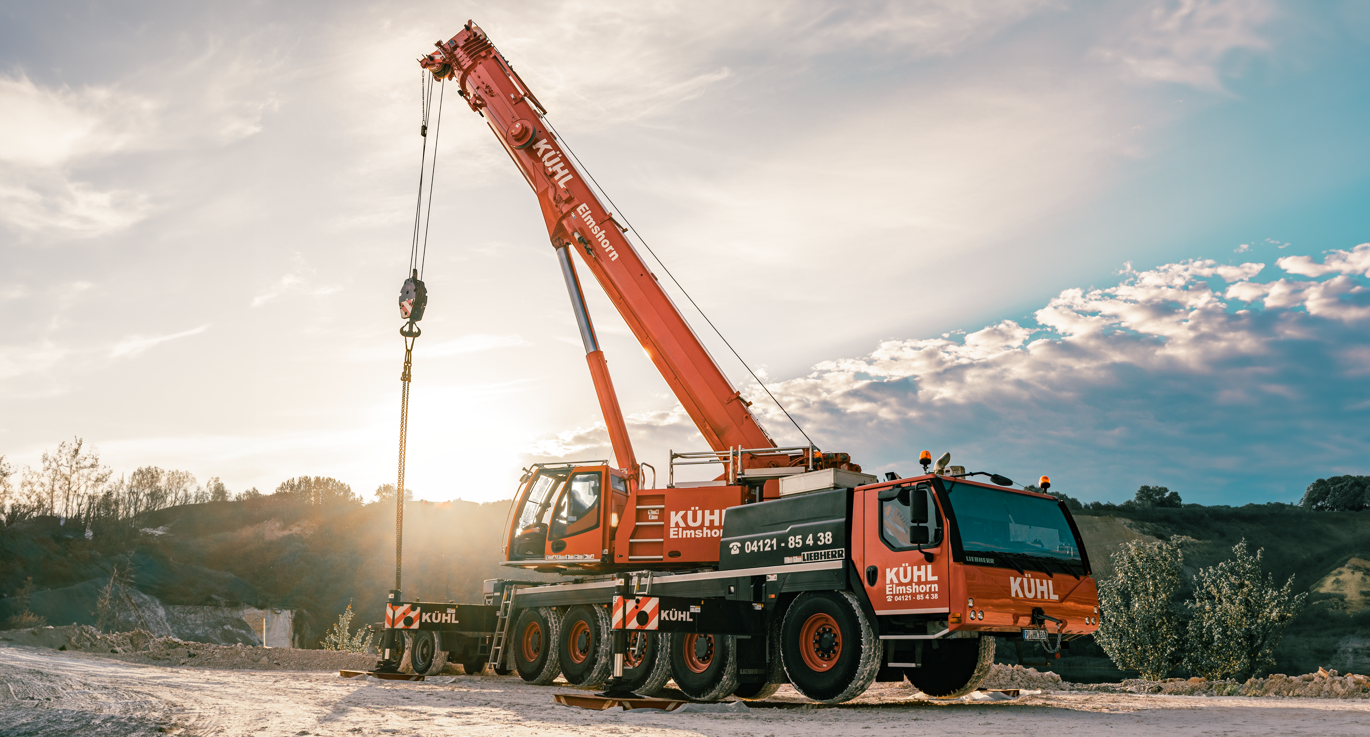 Kühl-Kranverleih-Elmshorn-Hamburg Roter Liebherr Mobilkran von KÜHL Kranverleih mit ausgefahrenem Teleskopausleger auf einer Baustelle. Im Hintergrund ein blauer Himmel mit Wolken. Der Kran steht in Geeshacht und soll einen Baukran demontieren von der Firma Manu Bau
